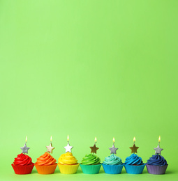 Photo of Delicious birthday cupcakes with burning candles on green background