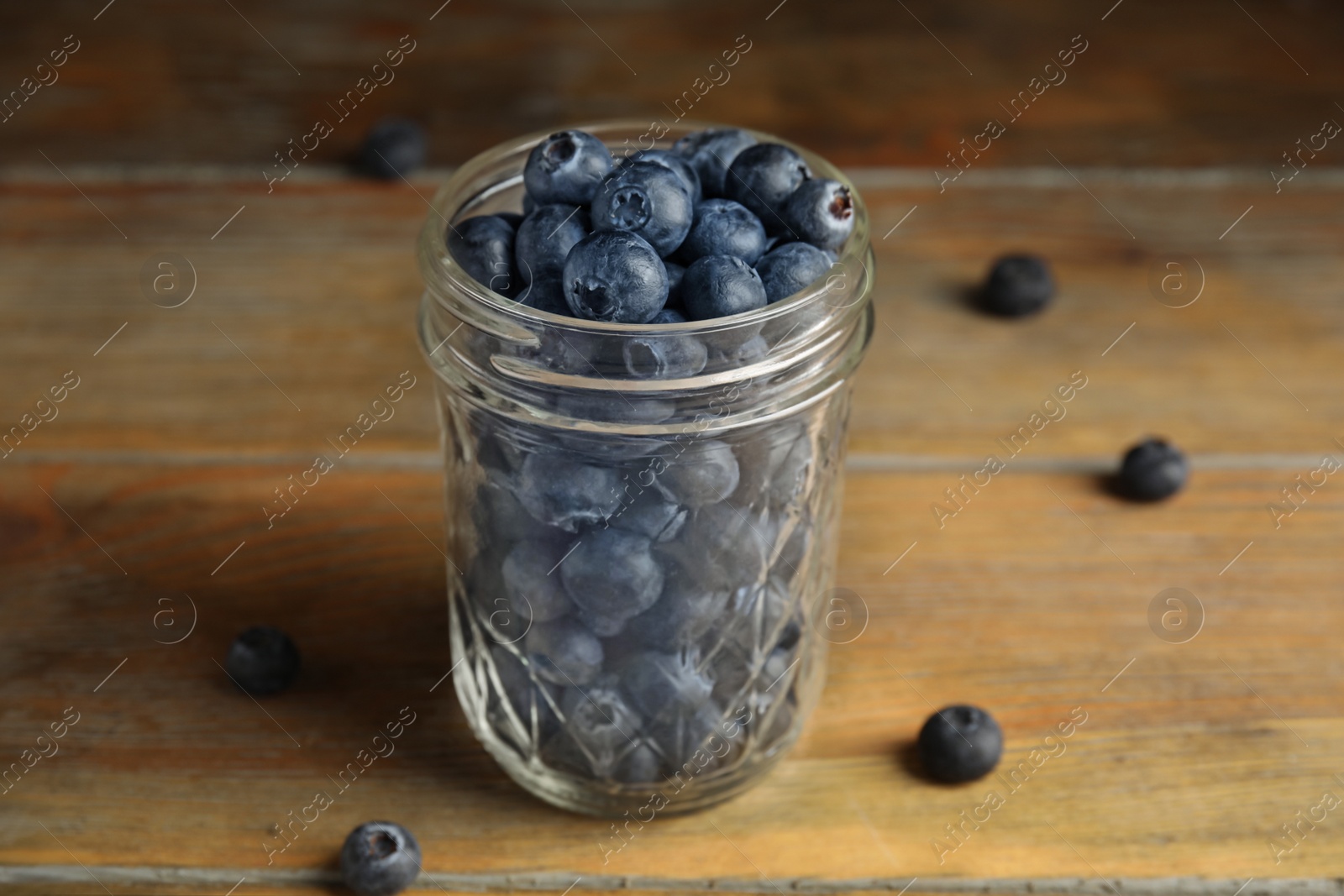 Photo of Tasty ripe blueberries in glass jar on wooden table