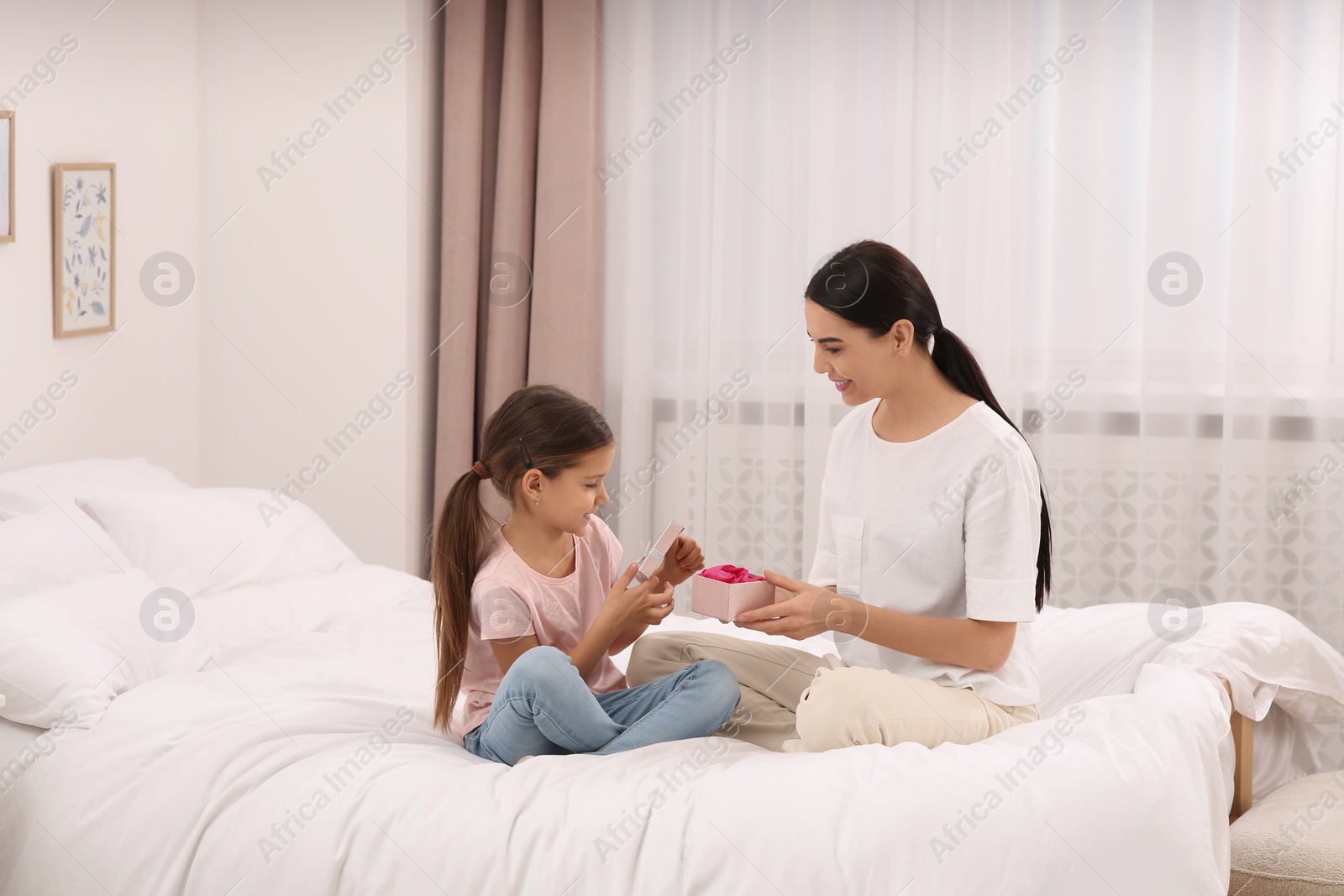 Photo of Daughter gifting happy woman gift box on bed at home. Mother's day celebration