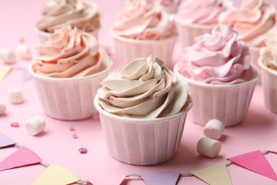 Photo of Delicious birthday cupcakes, bunting flags, marshmallows and sprinkles on pink background, closeup