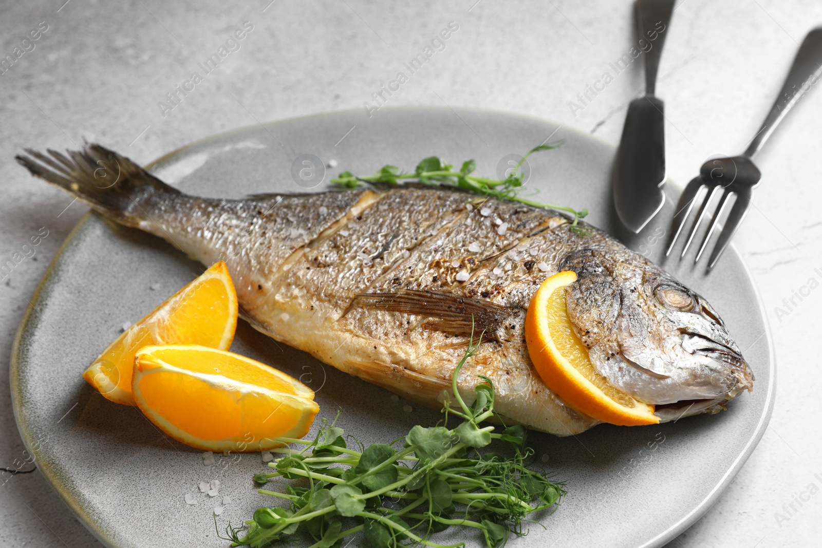 Photo of Seafood. Delicious baked fish served with orange and microgreens on light textured table, closeup