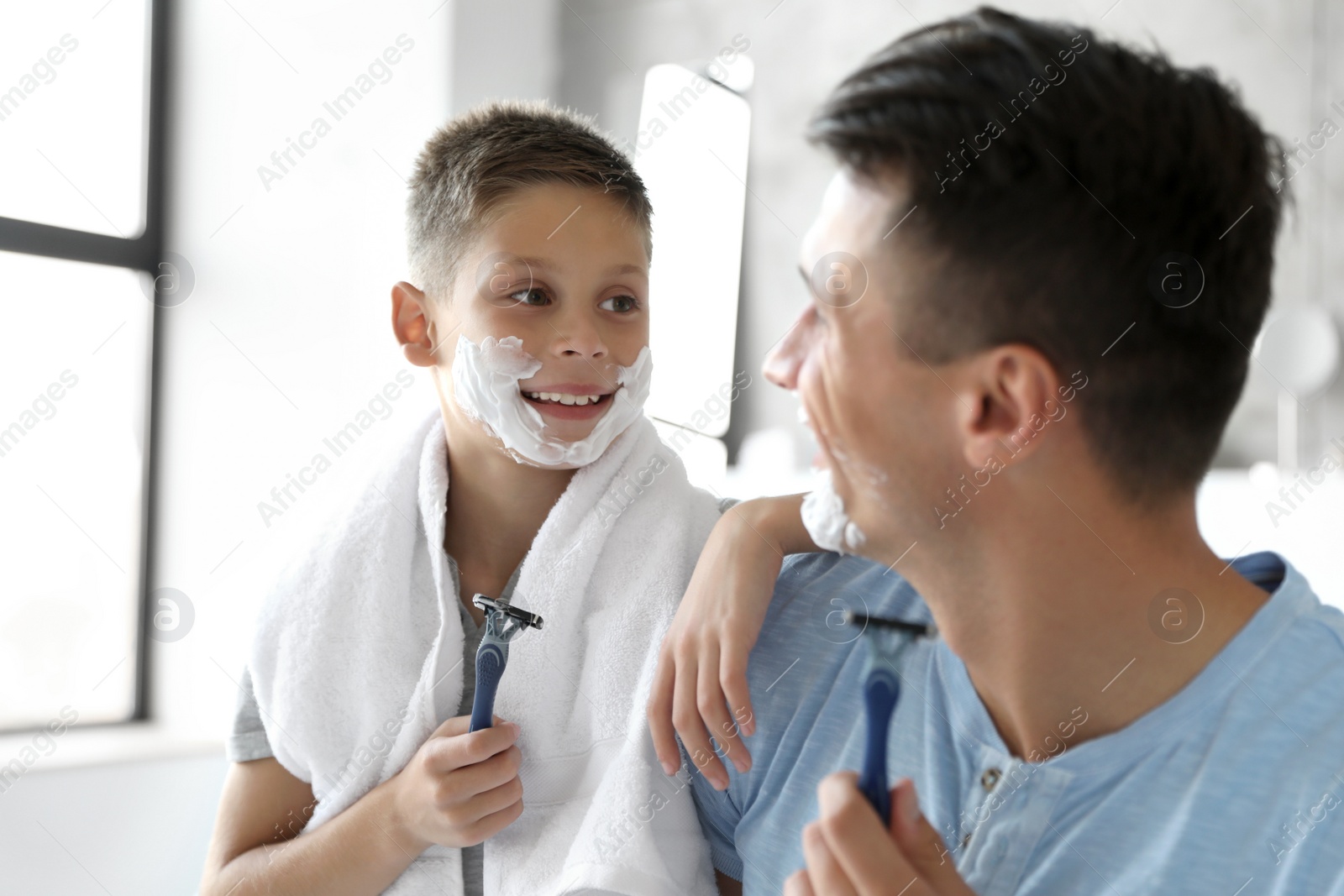 Photo of Happy father and son with shaving foam on their faces in bathroom