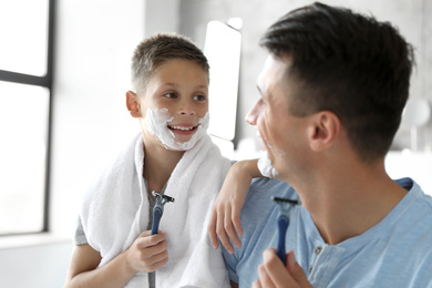 Happy father and son with shaving foam on their faces in bathroom