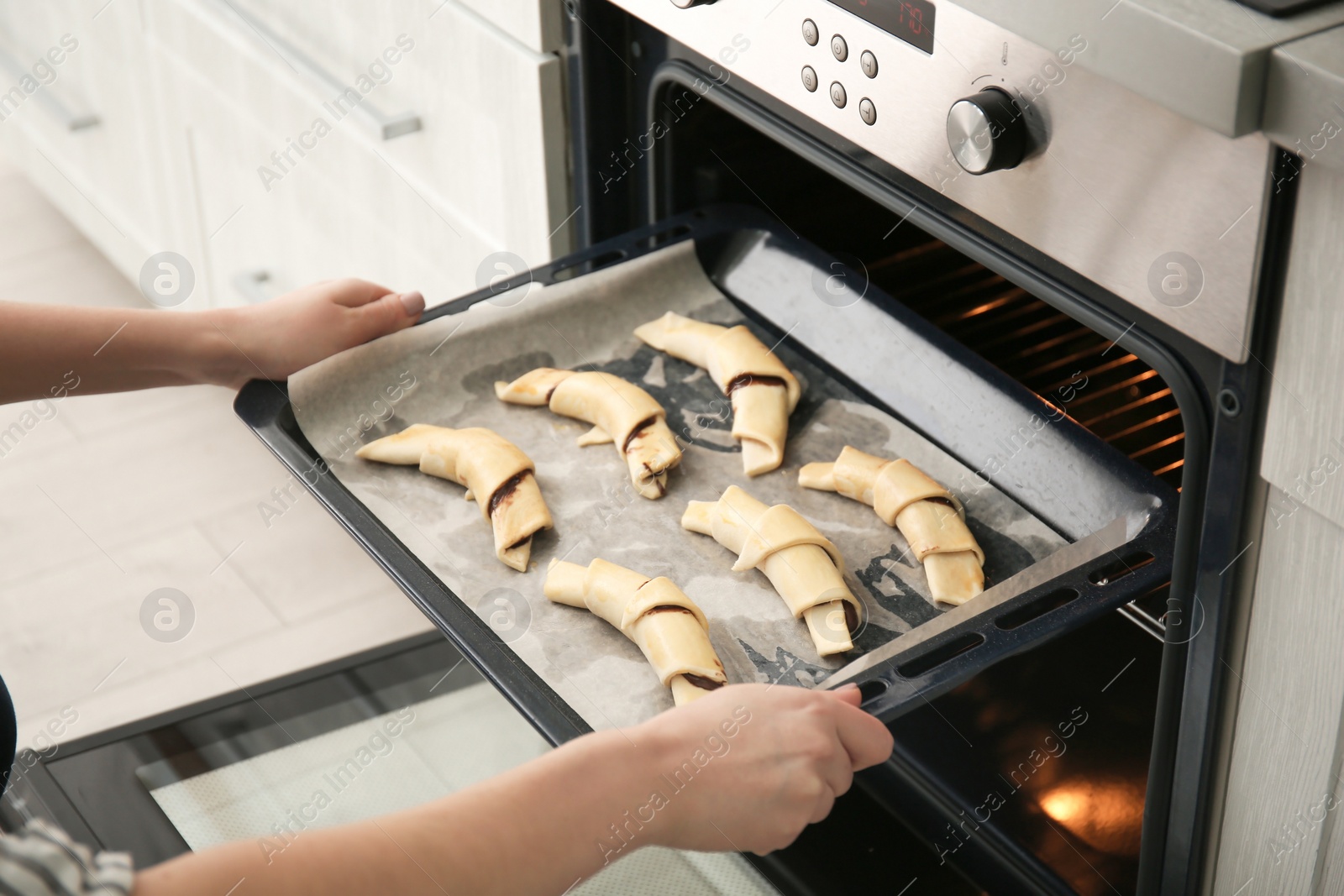 Photo of Woman putting baking sheet with raw croissants in oven, closeup