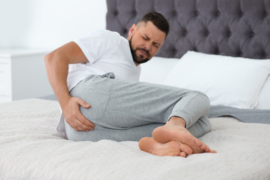 Photo of Man suffering from hemorrhoid on bed at home, focus on hand