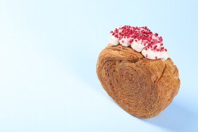 Photo of One supreme croissant with cream on light blue background, space for text. Tasty puff pastry