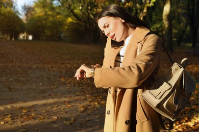 Emotional woman checking time while talking on smartphone in park. Being late concept