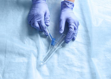 Photo of Doctor holding anoscope on light blue fabric, top view. Hemorrhoid treatment