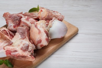 Photo of Cutting board with raw chopped meaty bones and basil on white wooden table, closeup. Space for text