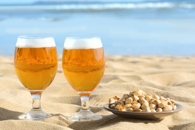 Glasses of cold beer and pistachios on sandy beach near sea