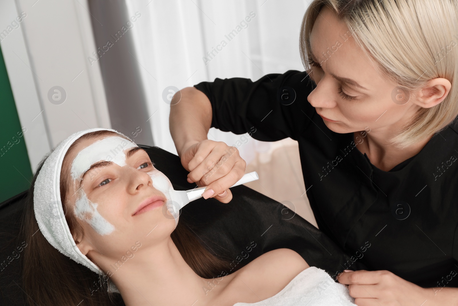 Photo of Cosmetologist applying mask on woman's face in clinic