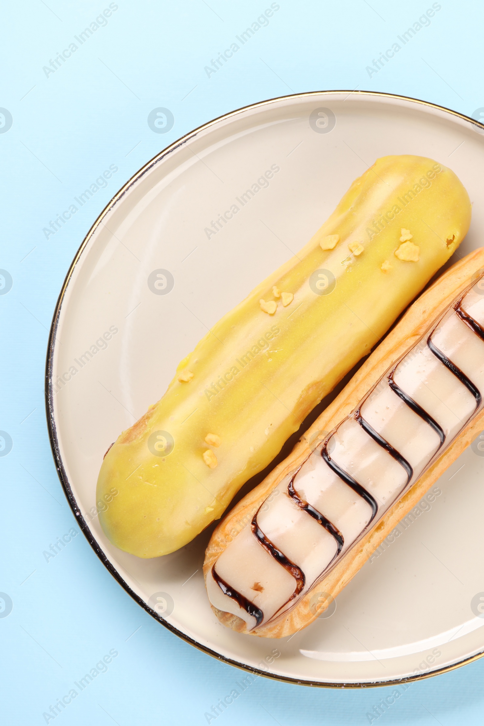 Photo of Delicious eclairs covered with glaze on light blue background, top view