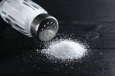 Photo of Organic salt in glass shaker on black wooden table, closeup. Space for text