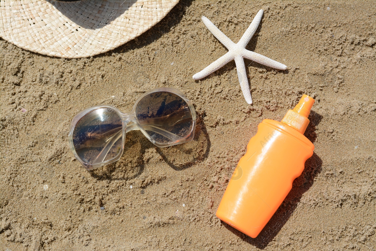 Photo of Blank bottle of sunscreen, starfish and beach accessories on sand, flat lay