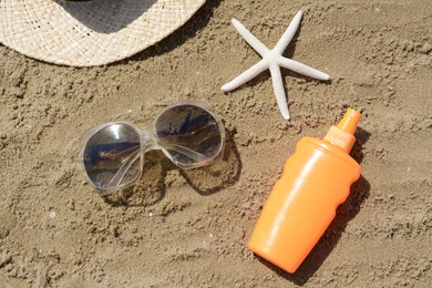 Blank bottle of sunscreen, starfish and beach accessories on sand, flat lay
