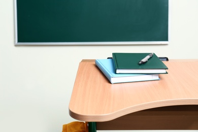 Photo of Wooden school desk with stationery near chalkboard in classroom