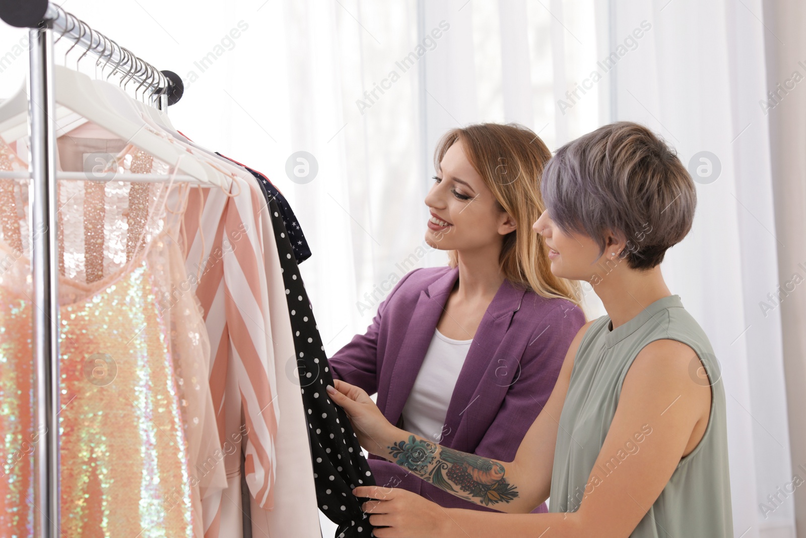 Photo of Young stylist helping client to choose trendy clothes in studio