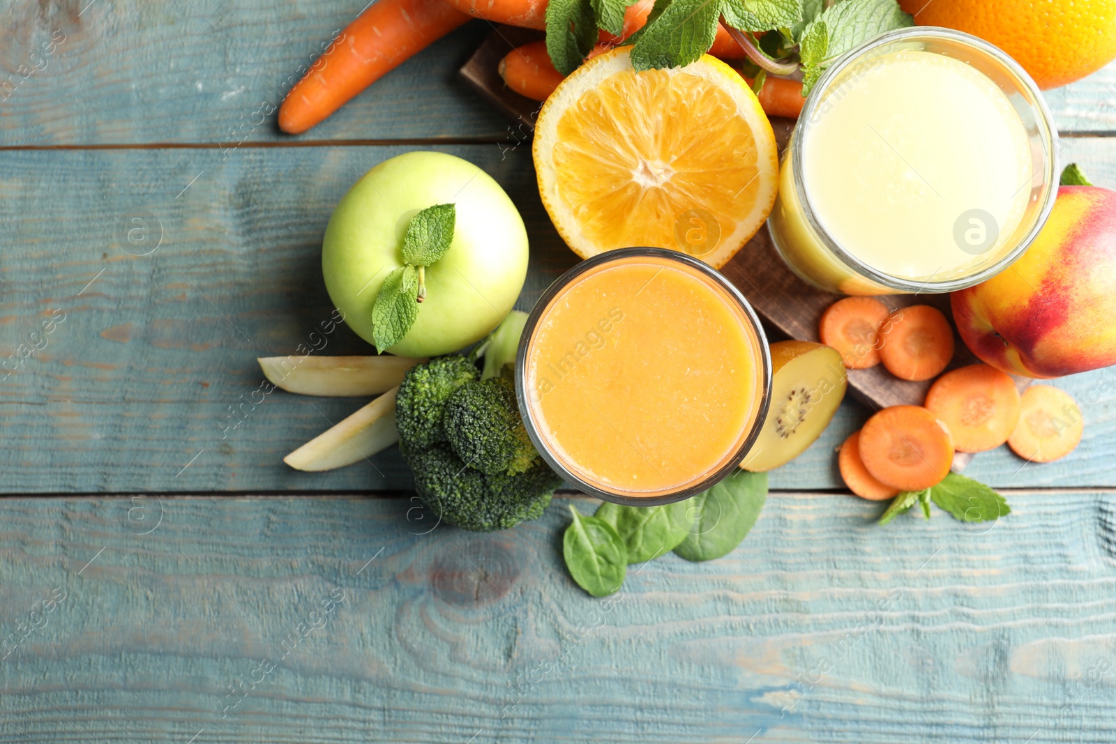 Photo of Glasses of delicious juices and fresh ingredients on blue wooden table, flat lay