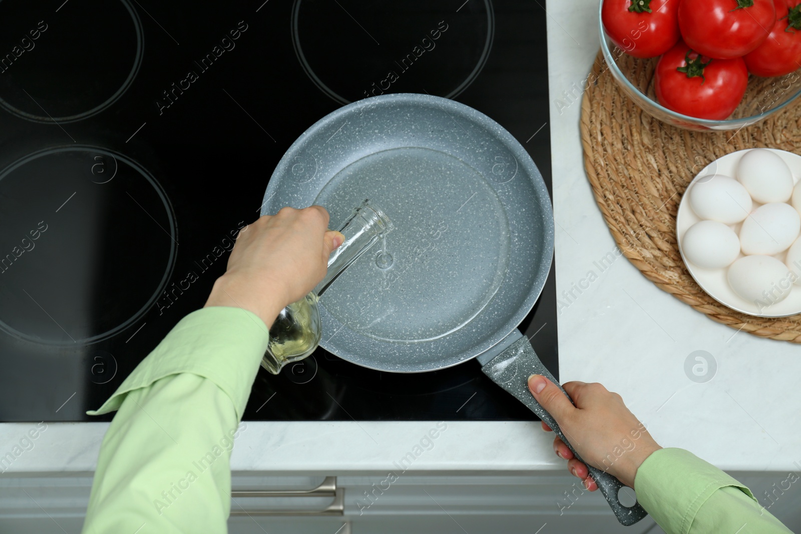 Photo of Woman pouring cooking oil from jug into frying pan in kitchen, top view