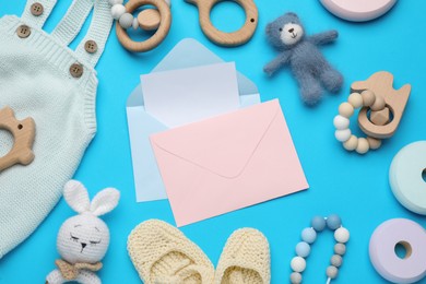 Baby shower party. Envelopes surrounded by stuff and toys for child on light blue background, flat lay