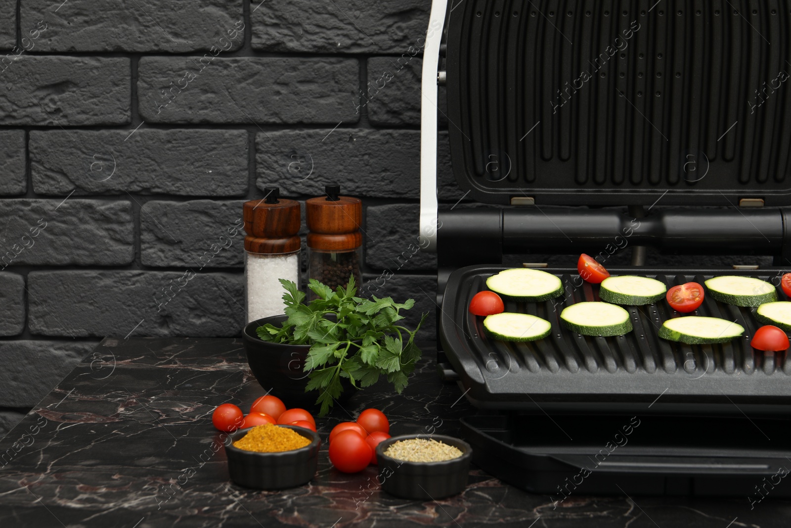 Photo of Electric grill with vegetables and spices on black marble table