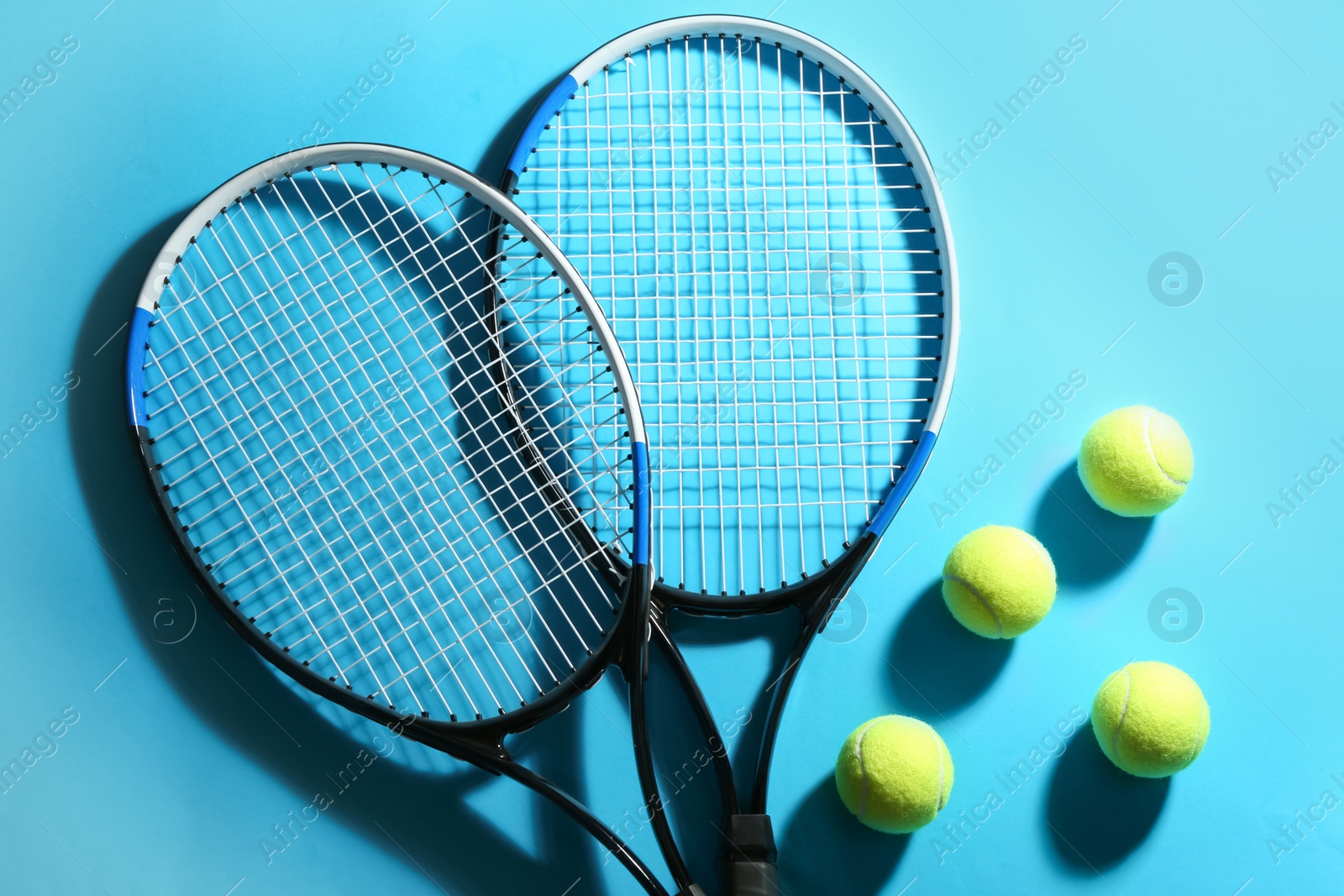 Photo of Tennis rackets and balls on blue background, flat lay. Sports equipment