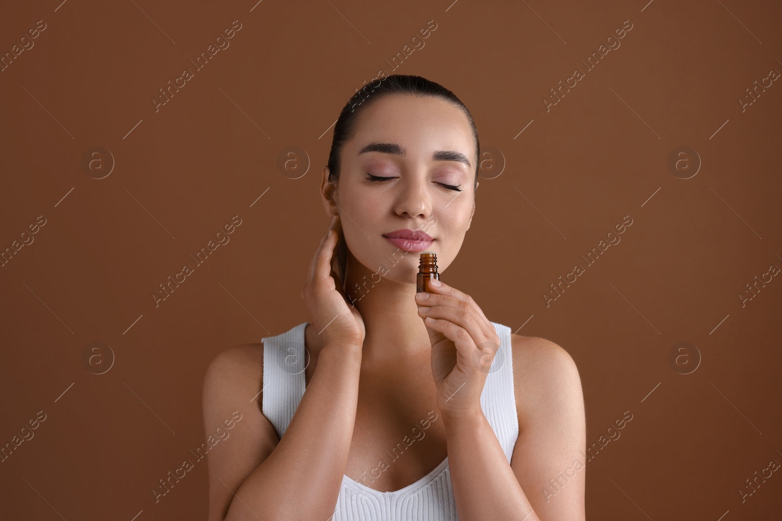 Photo of Beautiful young woman with bottle of essential oil on brown background