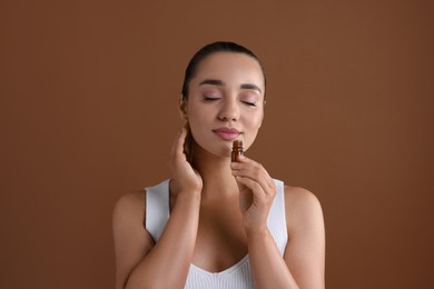 Beautiful young woman with bottle of essential oil on brown background