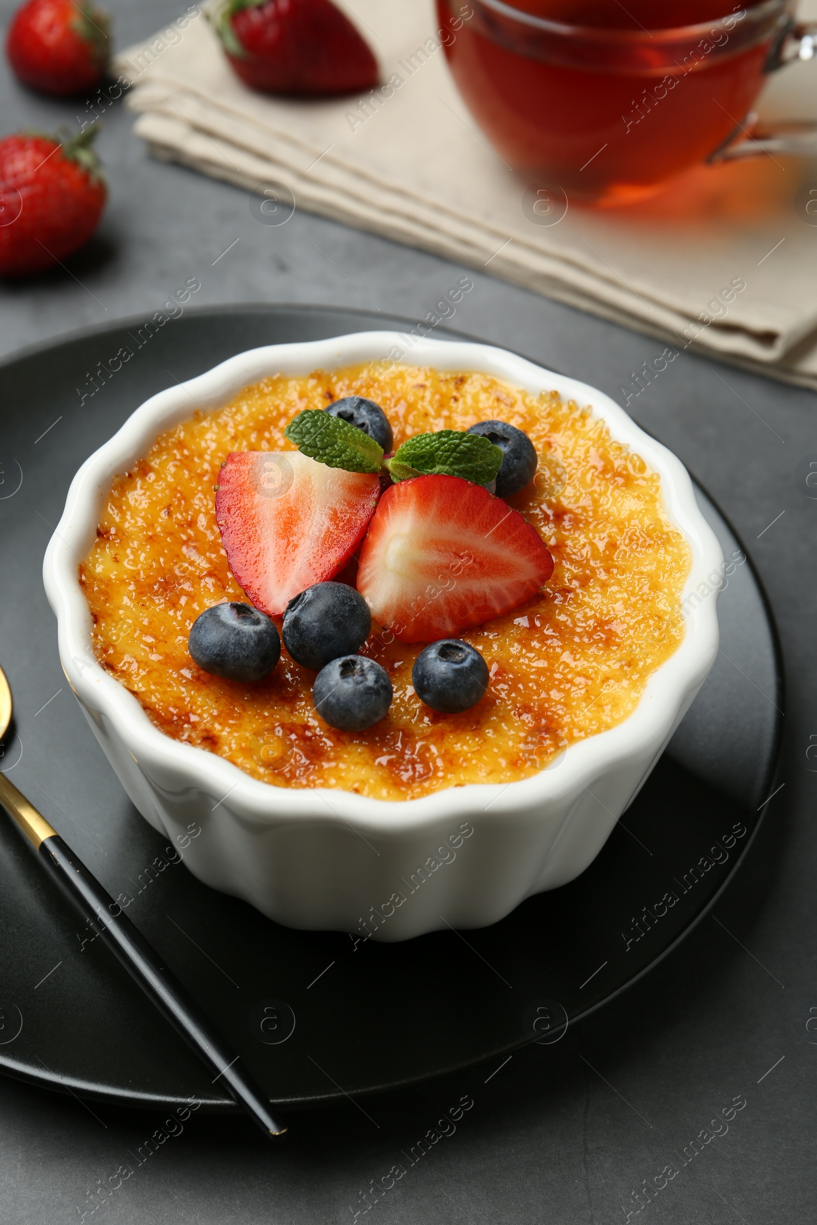 Photo of Delicious creme brulee with berries and mint in bowl on grey table, closeup