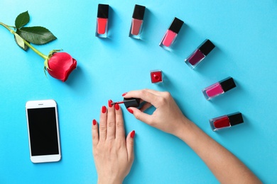 Woman applying bright nail polish on color background, top view