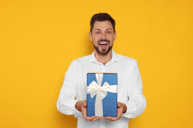 Happy man with gift box on yellow background