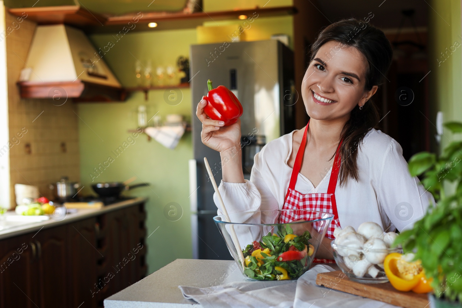 Photo of Young woman with fresh bell pepper and bowl of salad at countertop in kitchen, space for text