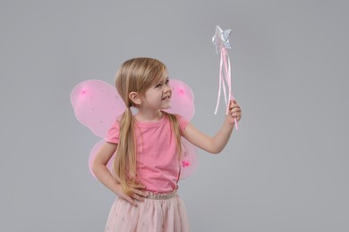 Photo of Cute little girl in fairy costume with pink wings and magic wand on light grey background