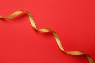 Photo of Beautiful golden ribbon on red background, top view