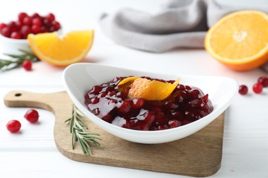 Photo of Fresh cranberry sauce with orange peel in bowl and rosemary on white wooden table, closeup