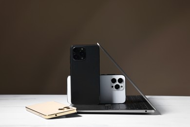 Modern laptop and smartphones on white table against brown background