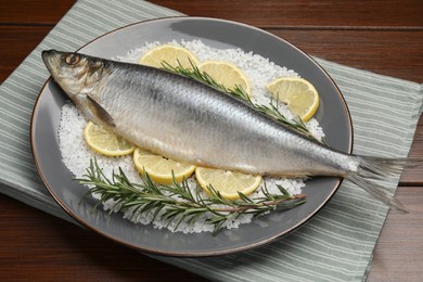 Photo of Delicious salted herring, rosemary, salt and lemon on wooden table