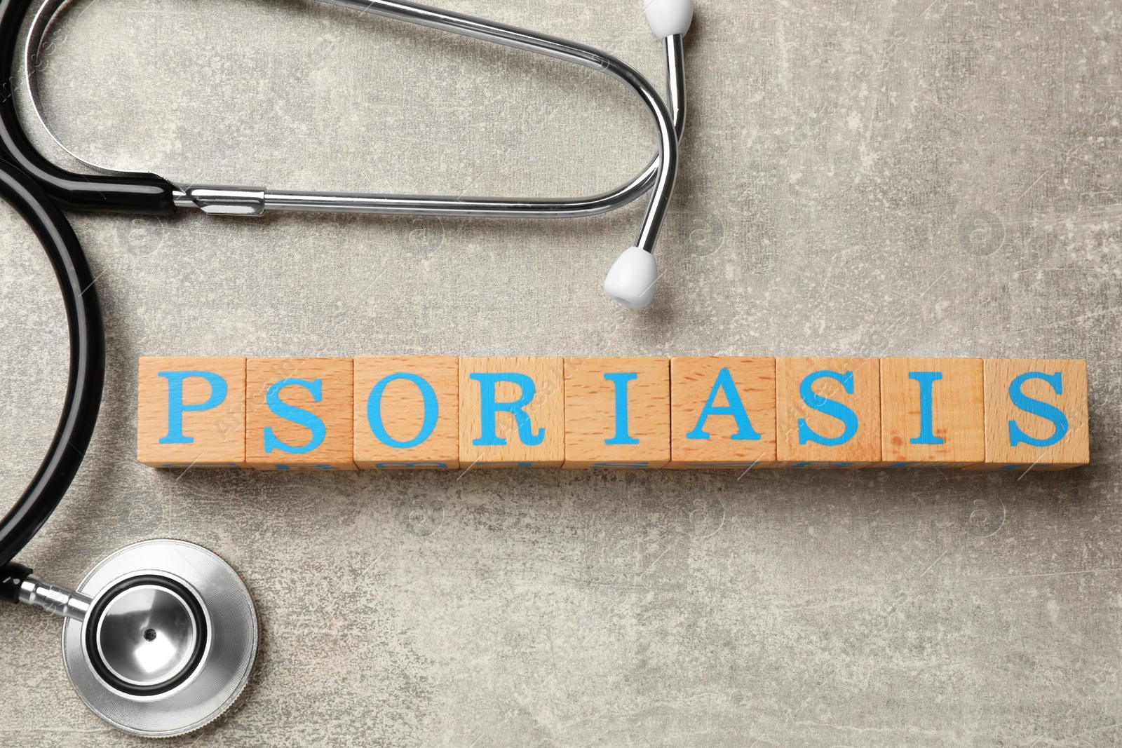 Photo of Word Psoriasis made of wooden cubes with letters and stethoscope on light gray textured table, flat lay