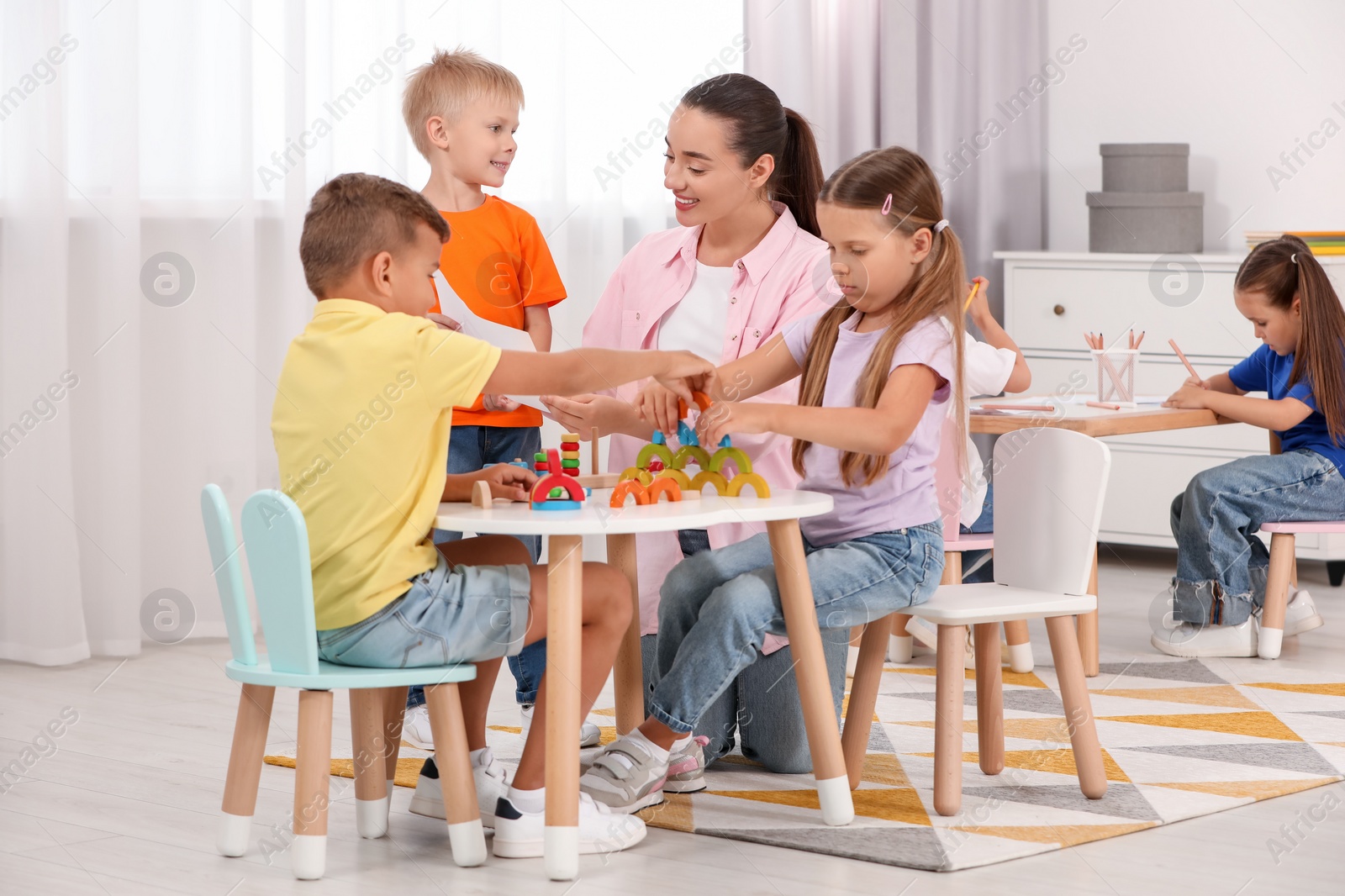 Photo of Nursery teacher and group of cute little children playing at desks in kindergarten. Activities for motor skills development