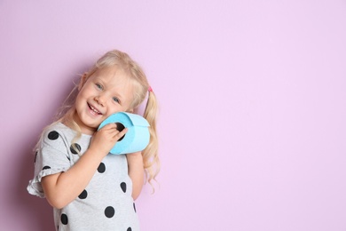 Photo of Cute little girl holding toilet paper roll on color background. Space for text