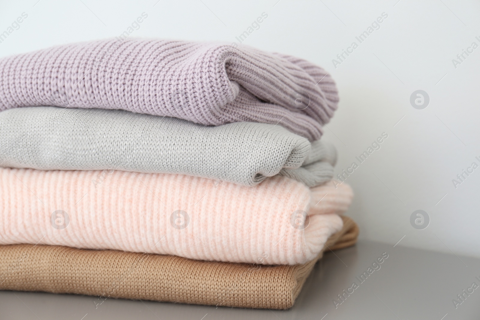 Photo of Stack of folded warm knitted sweaters on grey table, closeup