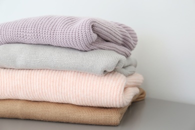 Stack of folded warm knitted sweaters on grey table, closeup