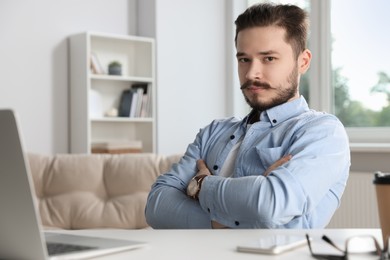 Photo of Serious man sitting at table near laptop in office