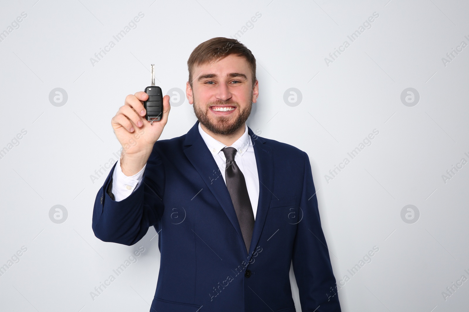 Photo of Happy young businessman with car key on grey background. Getting driving license