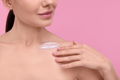 Photo of Woman with smear of body cream on her collarbone against pink background, closeup
