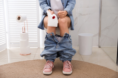 Woman holding toilet paper with blood stain in rest room, closeup. Hemorrhoid concept