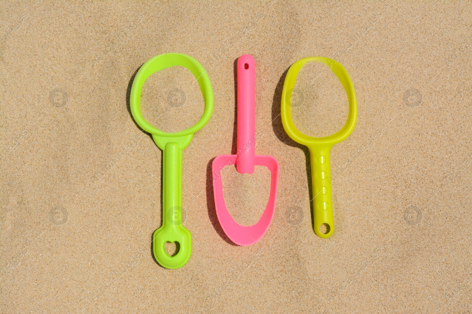 Photo of Colorful plastic shovels on sand, flat lay. Beach toys