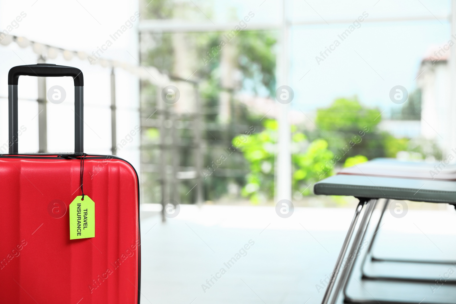 Photo of Red suitcase with TRAVEL INSURANCE label indoors, closeup. Space for text