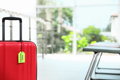 Red suitcase with TRAVEL INSURANCE label indoors, closeup. Space for text