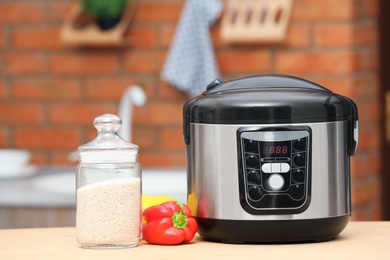 Photo of Modern electric multi cooker, jar of rice and peppers on table in kitchen